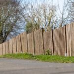 A landscape shot of a brown wooden fence of a mini forest with a clear blue sky